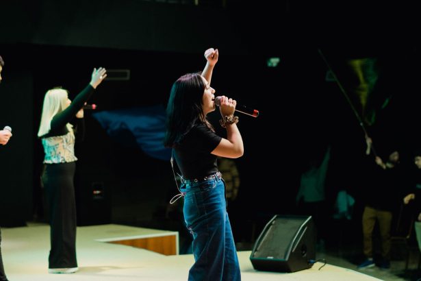 Cantora se apresenta ao vivo diante do público, com um braço levantado e um microfone à frente.