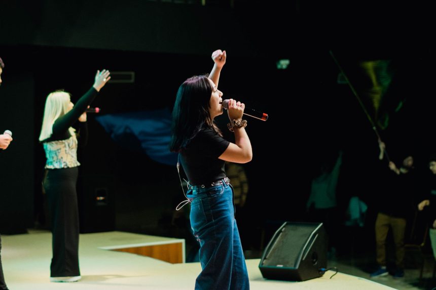 Cantora se apresenta ao vivo diante do público, com um braço levantado e um microfone à frente.