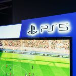 Estação de videogame com uma partida de futebol exibida na tela, acompanhada por um controle em primeiro plano.