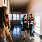 Adolescentes conversam e caminham por um corredor escolar bem iluminado.