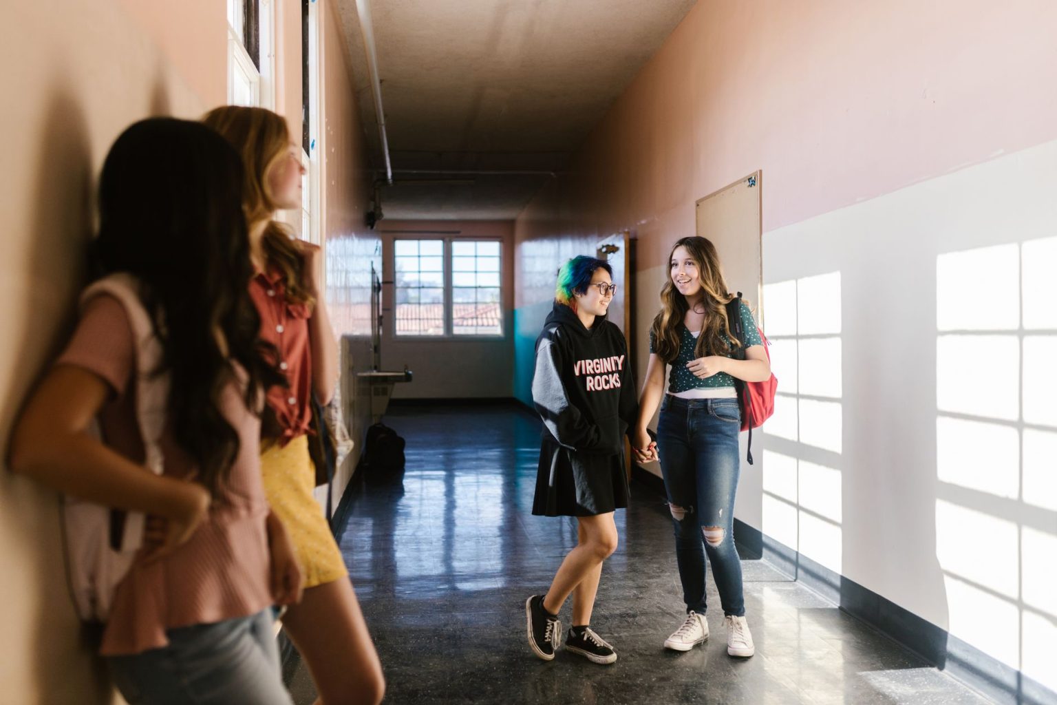 Adolescentes conversam e caminham por um corredor escolar bem iluminado.