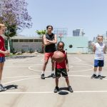 Grupo diverso de adolescentes reunido em uma quadra de basquete ao ar livre durante uma atividade recreativa